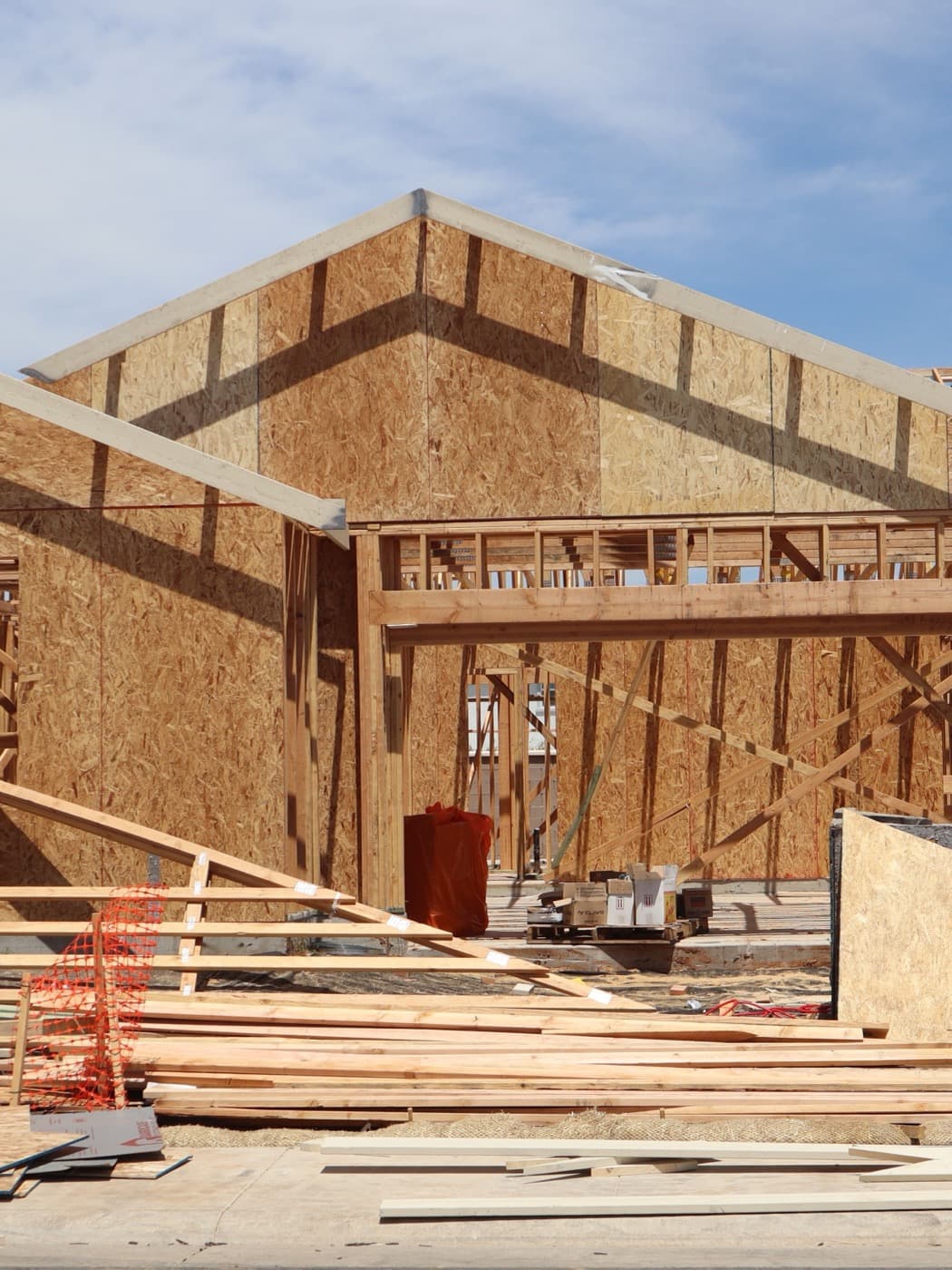 Wood-framed house under construction with lumber staged in the foreground