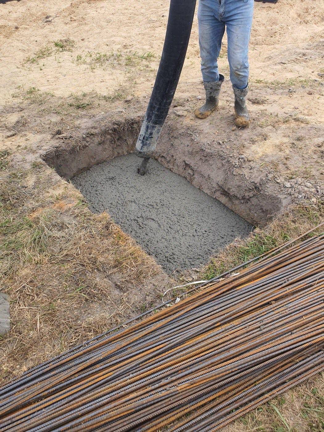 Concrete being poured into a foundation trench with rebar staged nearby